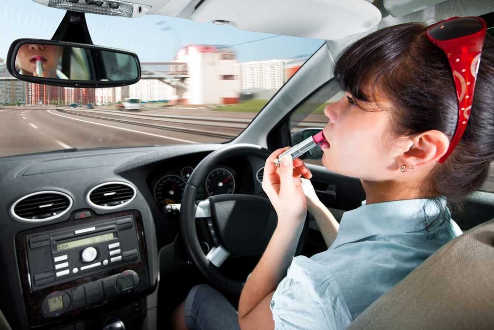 Woman applying makeup in a car mirror while finishing a quick everyday beauty routine